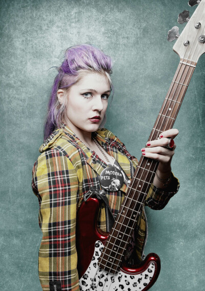 Nina Winkler Musikerin - Punk Bassistin hält Gitarre in der Hand, steht vor grüner Wand, lila Haare, Foto Peter Koehn - 2014 Foto Peter Koehn